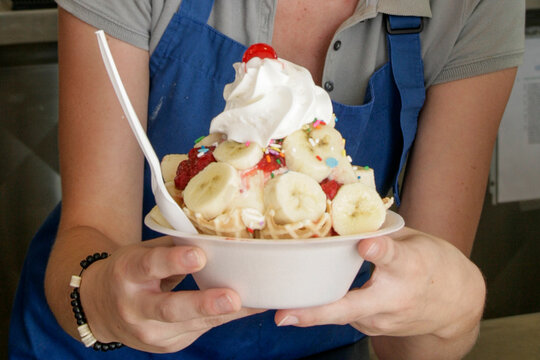 Woman holding banana split ice cream dessert with whipped cream and sprinkles