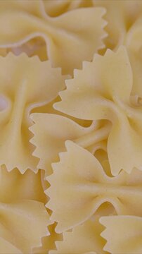 Uncooked bowtie pasta detail. Rustic pantry filled with dry pasta pieces. Closeshot of dry bowtie pasta showing scalloped edges and shadowed grains for food imagery