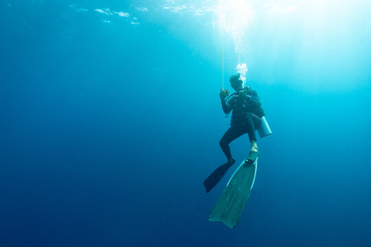 Diver exploring under clear blue water while using a buoy line for safety and navigation during an underwater activity