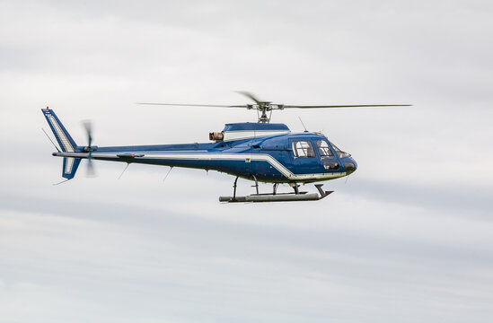 Blue helicopter flying over a grey sky - France
