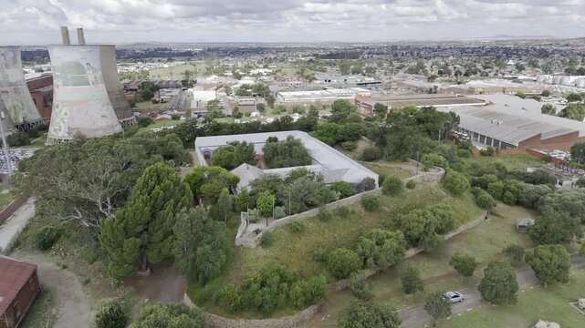 Drone orbits to the right over Queens Fort Military Museum with view of four towers of the power station on partially cloudy afternoon in Bloemfontein, South Africa