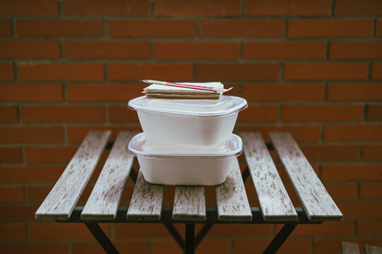 Dos envases de comida para llevar de cart&oacute;n con tapa de pl&aacute;stico sobre una mesa de terraza exterior. Concepto de comida para llevar, delivery y envase reciclable. 