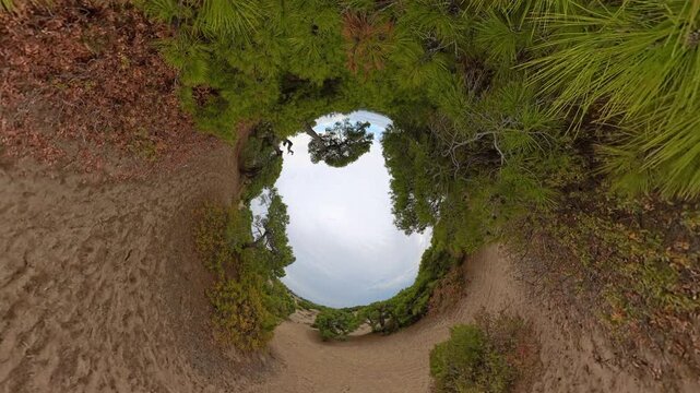 A 360-degree view twisting into a surreal tunnel effect captures a sandy path bordered by vibrant green foliage, leading toward an open sky