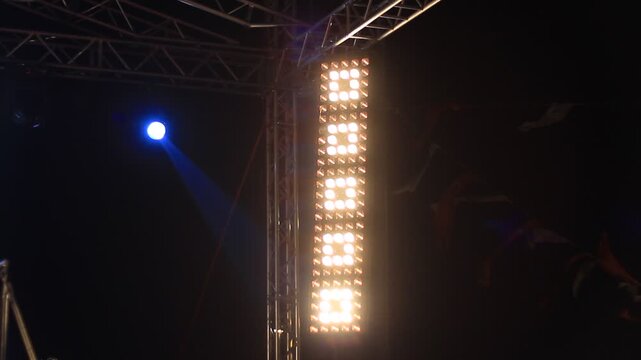 Stage lighting rig with bright LED panel and moving spotlights at night concert with smoke and lens flare effect