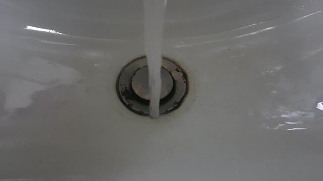 Close-up of running water from faucet hitting sink drain in bathroom. Static camera shows continuous water flow and clean indoor environment with minimal composition.