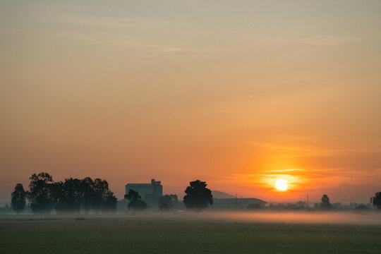 Sunrise over misty countryside with industrial silhouettes &mdash; a serene blend of nature and structure