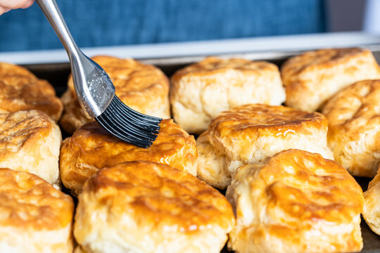 Butter being brushed on freshly baked biscuits on a baking sheet  