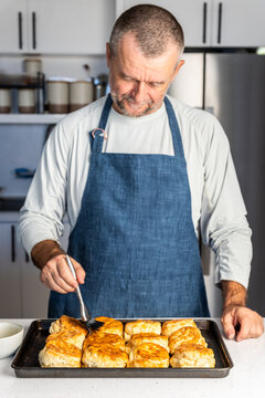 Man brushing butter on fresh biscuits in a kitchen 