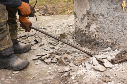 Horizontal medium shot: worker breaking concrete on a well with a crowbar from the side.