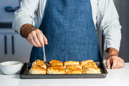 Man brushing butter on fresh biscuits in a kitchen 