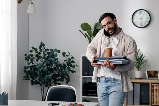 Young man multitasking while talking on phone and carrying work items