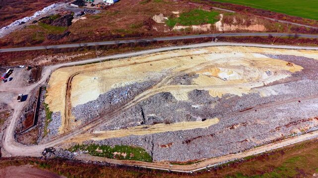 Large open-air garbage dump with sandy soil tracks and surrounding green fields. Aerial view of municipal solid waste landfill site.