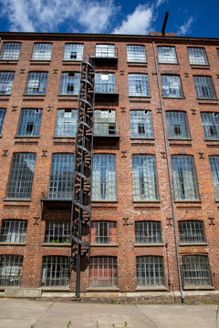 Alte verlassene Fabrik aus rotem Backstein mit gro&szlig;en Fenstern und Feuertreppe unter blauem Himmel