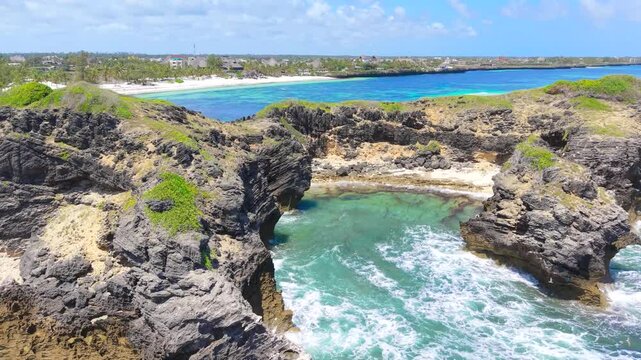 Aerial view of waves crashing against dark coral rock formations and turquoise water near a white sand beach in Watamu, Kenya.