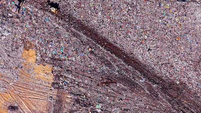 Overhead shot of diverse household waste being processed by heavy machinery. Abstract pattern of waste materials at landfill site with birds flying over garbage.