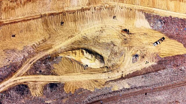 Aerial top view of heavy machinery and trucks moving sandy soil over a waste disposal area. Excavation and soil management at landfill facility.
