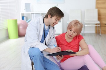 Obraz premium Senior woman and physiotherapist with clipboard indoors