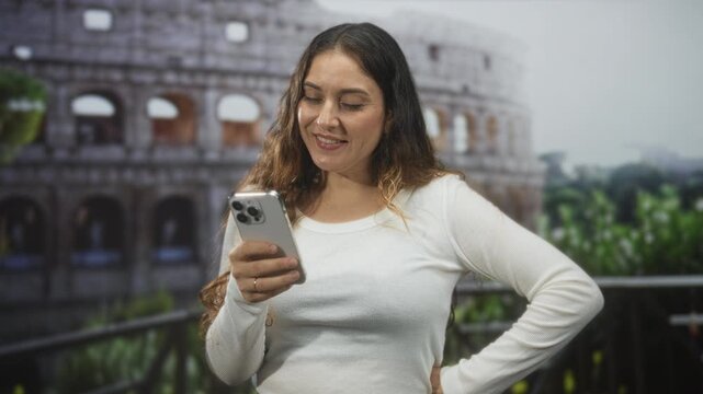 Woman holding smartphone and checking messages with hand on hip in a studio with colosseum backdrop; serene connection.
