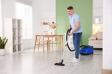 Fototapeta premium Smiling man cleaning floor with vacuum cleaner at home