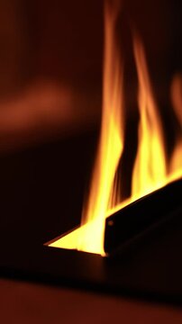 Tall amber flames rise from a metal burner in a linear inset fireplace, reflecting on a dark hearth. Slow, flickering motion and warm bokeh suggest an alpine lounge.