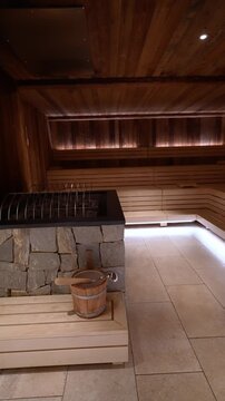Vertical interior shots show tiered benches, stone clad heater with guard, wooden bucket and ladle, warm backlighting, and reclaimed wood in an Alpine spa.