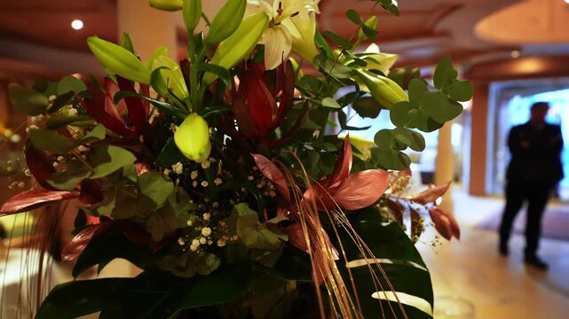 Ornate floral centerpiece with white lilies, eucalyptus, baby's breath, and copper leaves sits in an Ischgl, Austria hotel lobby as a figure passes by near doors.