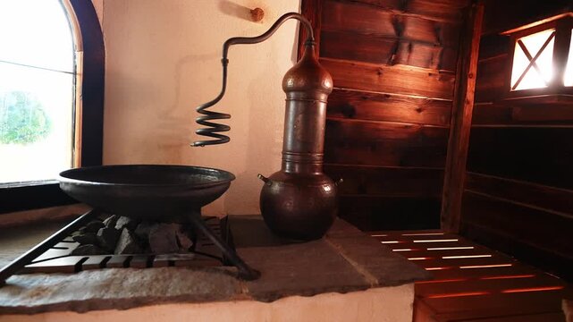 Warm interior shows copper alembic, sauna stones, arched leaded window, and wood walls in a luxury  hotel spa, Austria, as the camera pans to the spiral condenser.