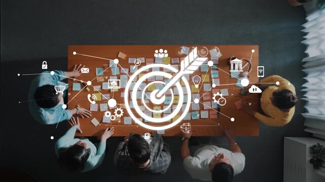 Aerial view of a diverse team collaborating around a table with digital icons representing strategy, goals, and communication in an inspiring office environment. Raster