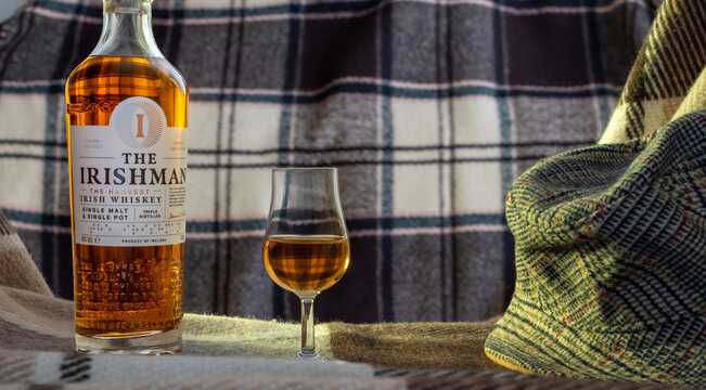 The Irishman Irish Whiskey bottle with a glencairn glass and a traditional flat cap on a wool plaid. Warm lifestyle photography with cozy heritage vibes. Ukraine, Zhytomyr, March 29, 2026