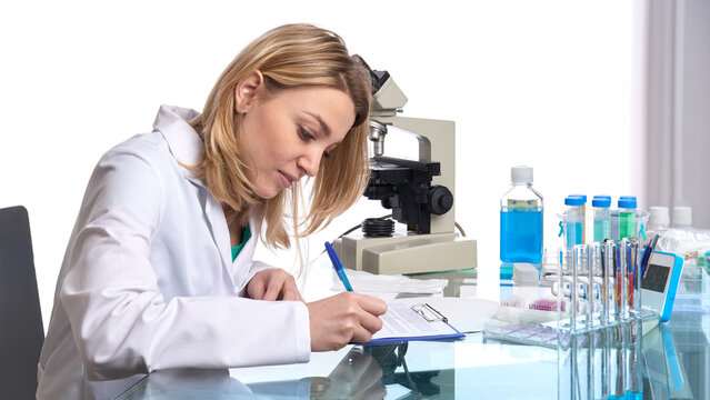 Young european female scientist with compound microscope taking notes in modern laboratory