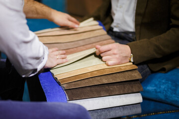 Two men collaborate, choosing from a swatch book of upholstery fabrics for interior design. Concept for interior design, home renovation, and making a choice. Seller and buyer.