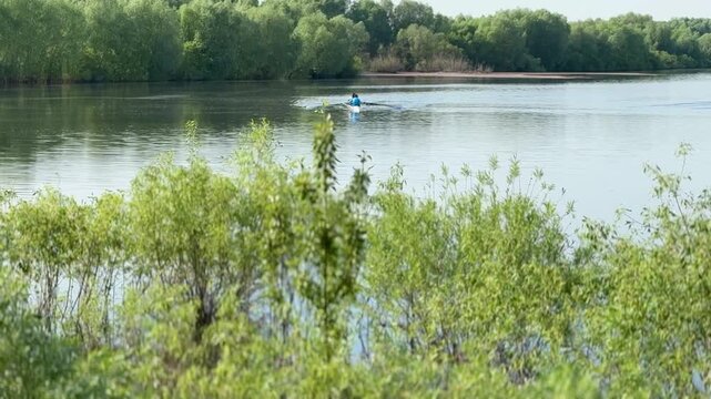 Kayakers training on river water in summer, athlete crew practicing paddling sprints across calm reflective surface, green.