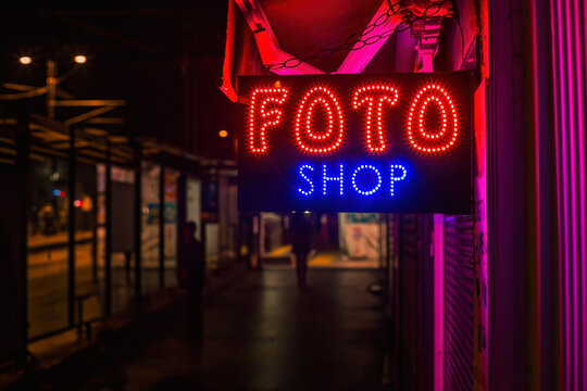 Photo shop Sign Glowing Over Empty City Street at Night With Pink and Blue Neon Lights
