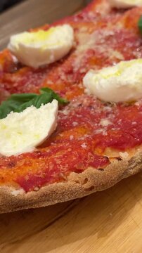 rectangular Italian pizza with tomato, cheese, and basil. Woman with brown manicure pulls apart a sliced piece. Rustic street food scene in Italy, fresh and appetizing.