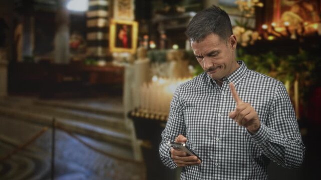 Man with moustache checks smartphone and points index finger with furrowed brow in ornate building near candles and rope barriers; quiet concern.
