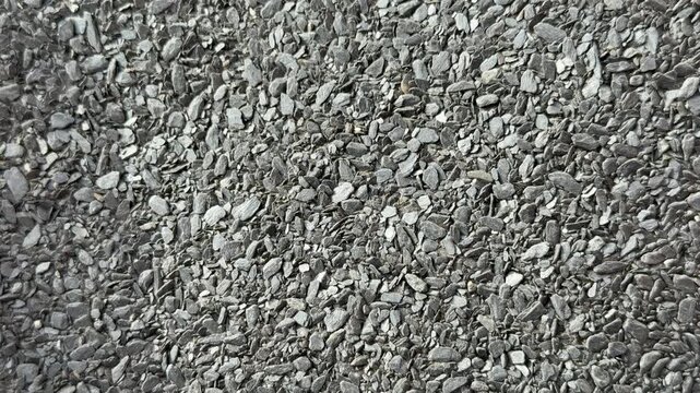 Close-up rolled roofing granules texture, coarse mineral surface on bitumen membrane, grey aggregate fragments, protective coating.