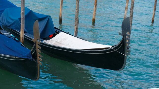 Gondolas moored in venice, italy, gently rocking on water. Traditional venetian gondolas, covered with blue cloth, rest peacefully on the water's surface, their ornate ferro and oarlocks