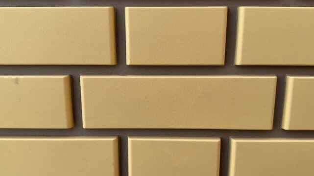 Facade panel closeup showing beige brick cladding with rectangular tiles, visible mortar joints and textured sandy finish.