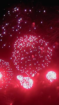 A vibrant pyrotechnic display explodes over the dark night sky. Red, white, and green bursts of light illuminate the night, creating patterns and a sense of grand celebration.