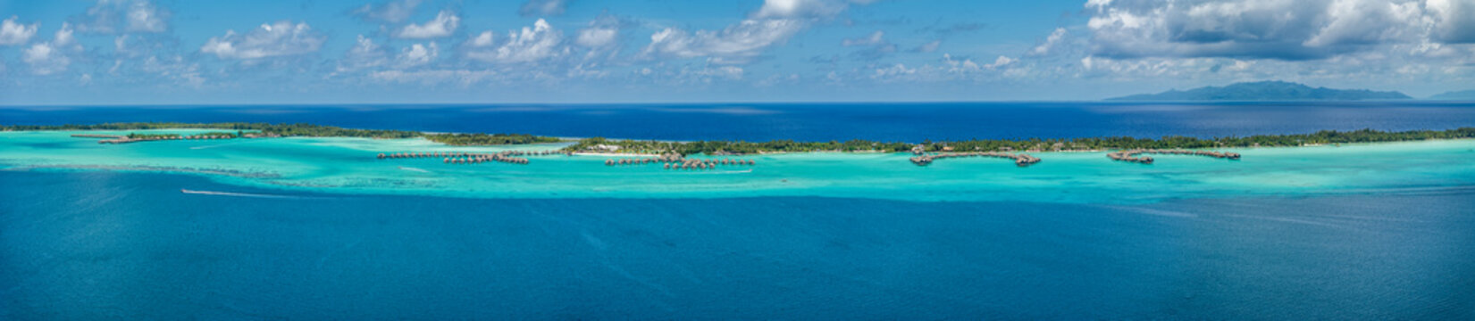 panoramic aerial landscape view of parts of Piti Aau and Motu Piti A'au Atoll as part of Bora Bora island with resorts and bungalows in bright turquoise blue water and Taha'a Island in the background 