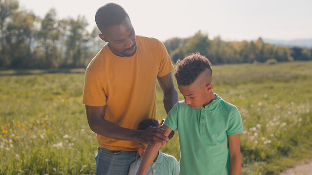 Father paying attention to sun protection for his two sons during summer outdoor activities, applying sunscreen to them.