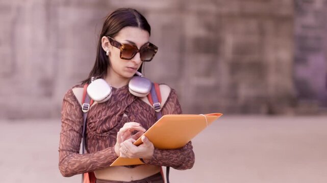 Young female student checking documents walking outdoors