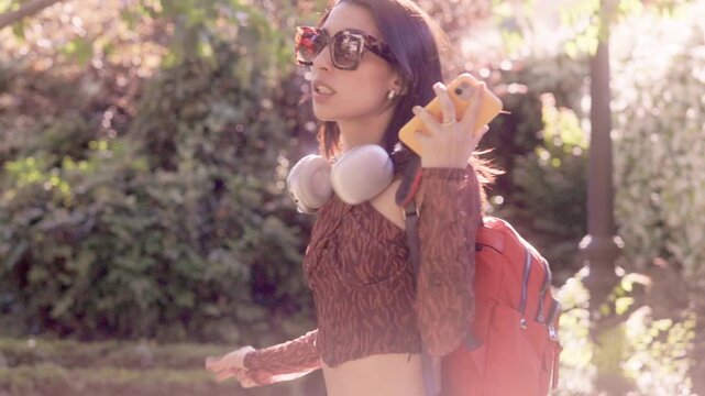 Happy young woman listening to music and dancing in a sunny park