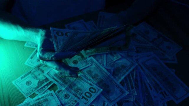 A woman playfully fans herself with a handful of dollar bills under dramatic blue lighting, then tosses them onto a stack of scattered money on the table, creating a scene of extravagance