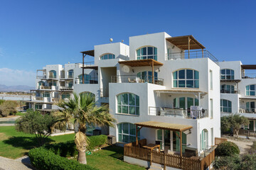 Fototapeta premium Sunny coastal villas with modern architecture near the serene beach at midday under a clear blue sky.