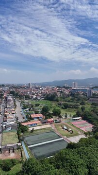 Vista a&eacute;rea de cidade com bairros residenciais, ruas, &aacute;reas verdes, quadras esportivas e montanhas ao fundo, destacando paisagem urbana e natureza em regi&atilde;o metropolitana brasileira.