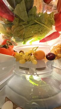 Vertical video. A 360-degree view inside a refrigerator showcases vibrant fruits, vegetables, and eggs in an organized and bright setting, creating a seamless loop of rotating motion