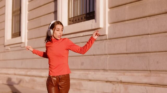 Carefree young woman dancing with headphones at sunset