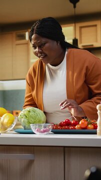 Black food vlogger reading live comments from the audience, recording a livestream on smartphone with tripod as stabilizer in the kitchen. Meal prep cooking vlog for social media.