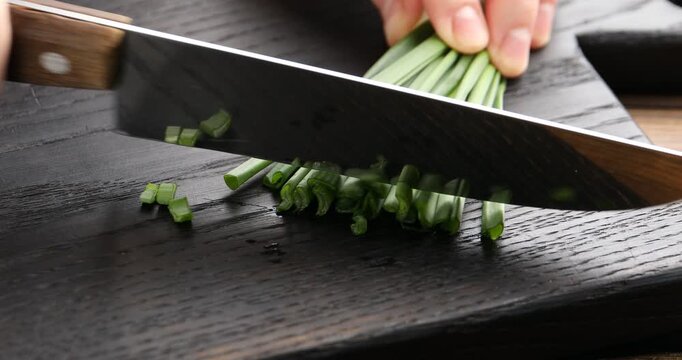 Woman cutting fresh green onion at table, closeup